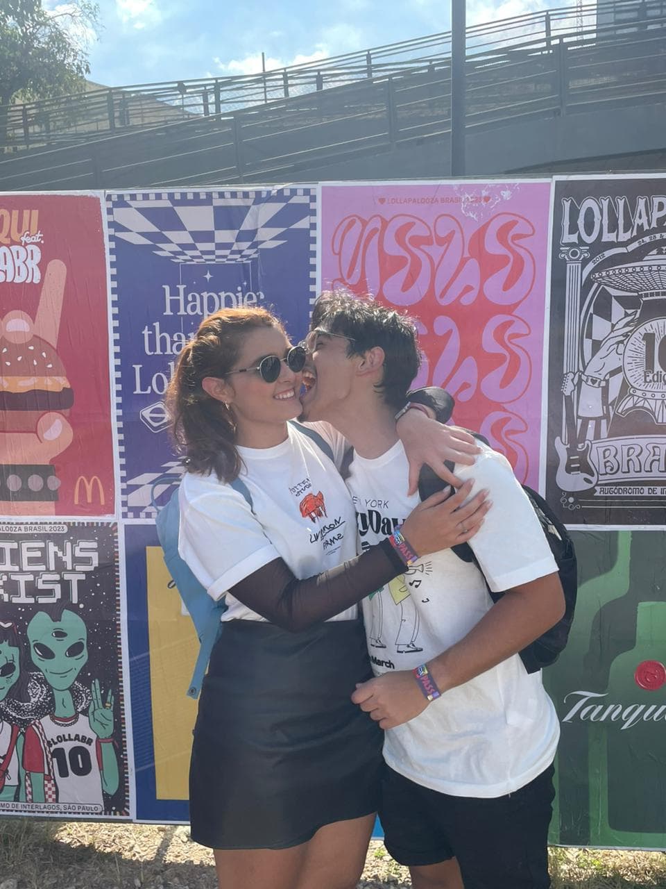 Lucas e Marina abraçados em frente aos cartazes do Lollapalooza