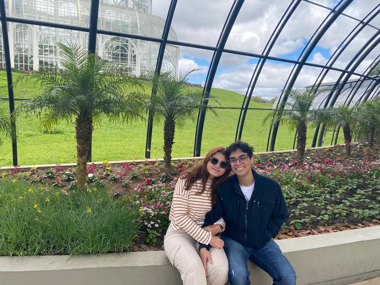 Lucas e Marina sentados em frente à estufa do Jardim Botânico
