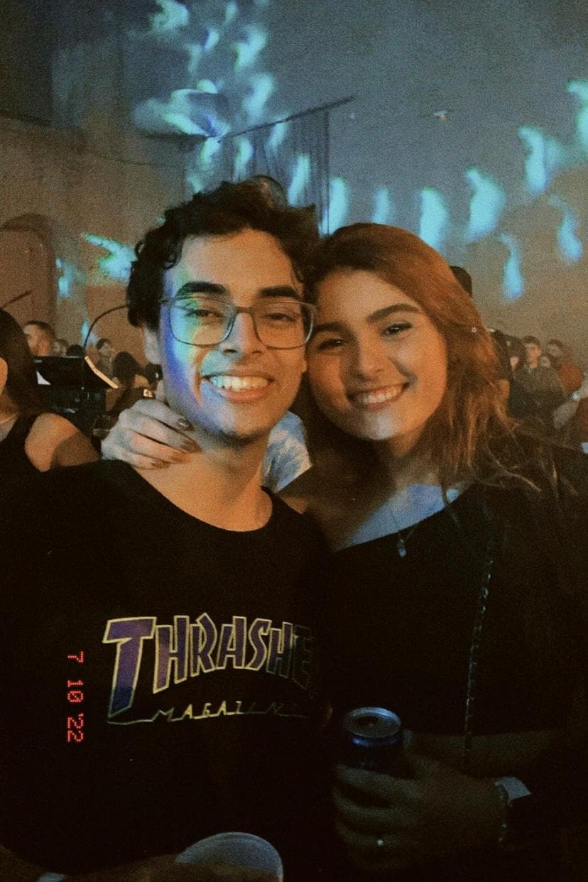 Lucas e Marina abraçados sorrindo em um show com luzes ao fundo